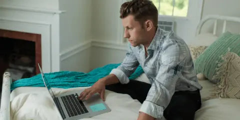 Man researching mattresses on computer, sitting on a Jamestown Mattress in his bedroom.